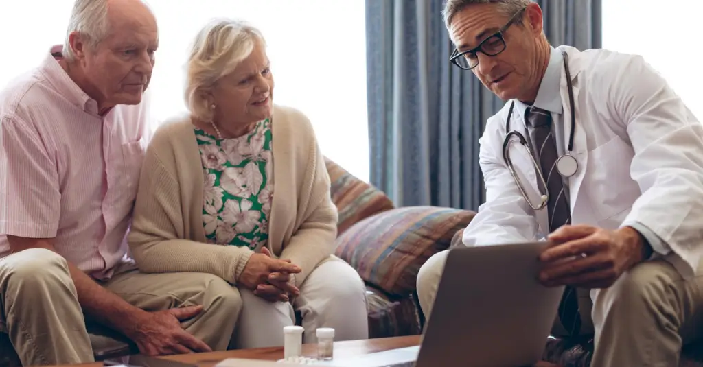Doctor reviewing Medicare Advantage Plan options on a laptop with a senior couple, discussing healthcare choices for 2026.