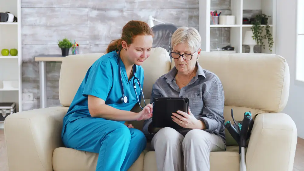 Home health nurse assisting elderly patient with digital medical records on a tablet - Human Medical Billing.