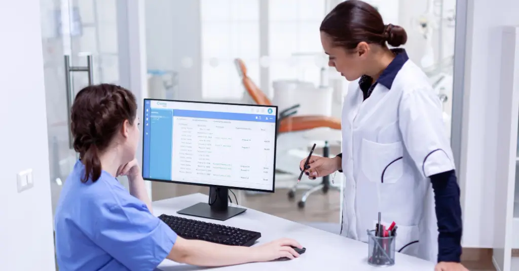 Two healthcare professionals reviewing billing data on a computer in a clinic.