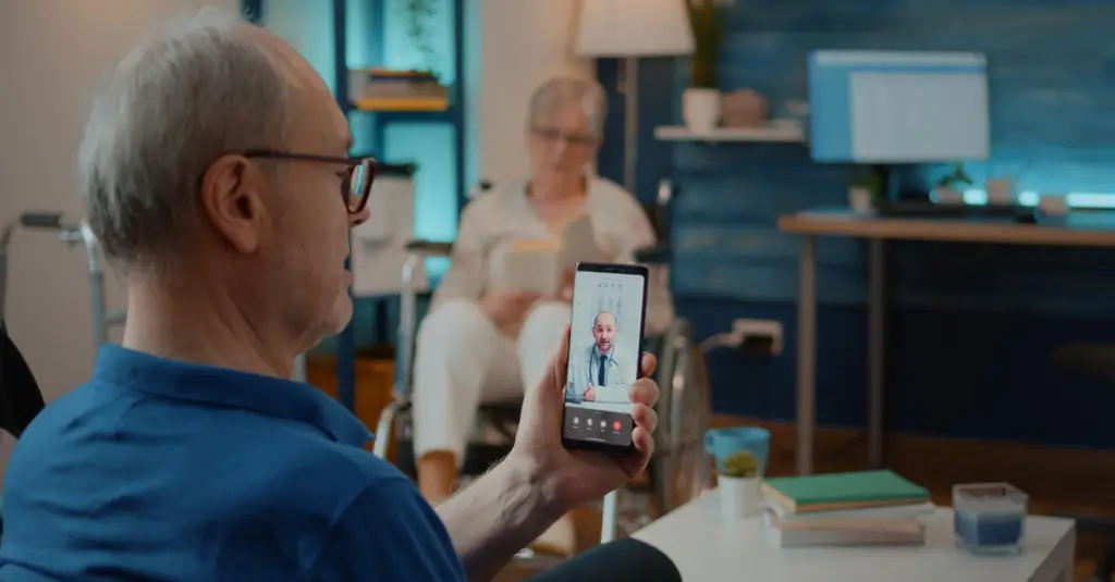 Patient holding a smartphone during a telehealth video visit with a physician, illustrating virtual direct supervision in healthcare.